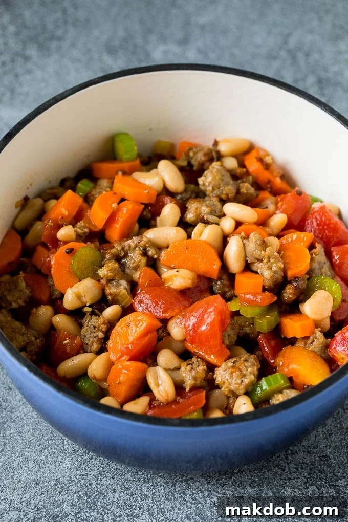 Soup Ingredients Simmering Together A vibrant mix of cannellini beans, diced tomatoes, tender vegetables, and savory Italian sausage simmering together in a large pot, creating the rich base for Tuscan White Bean Soup.