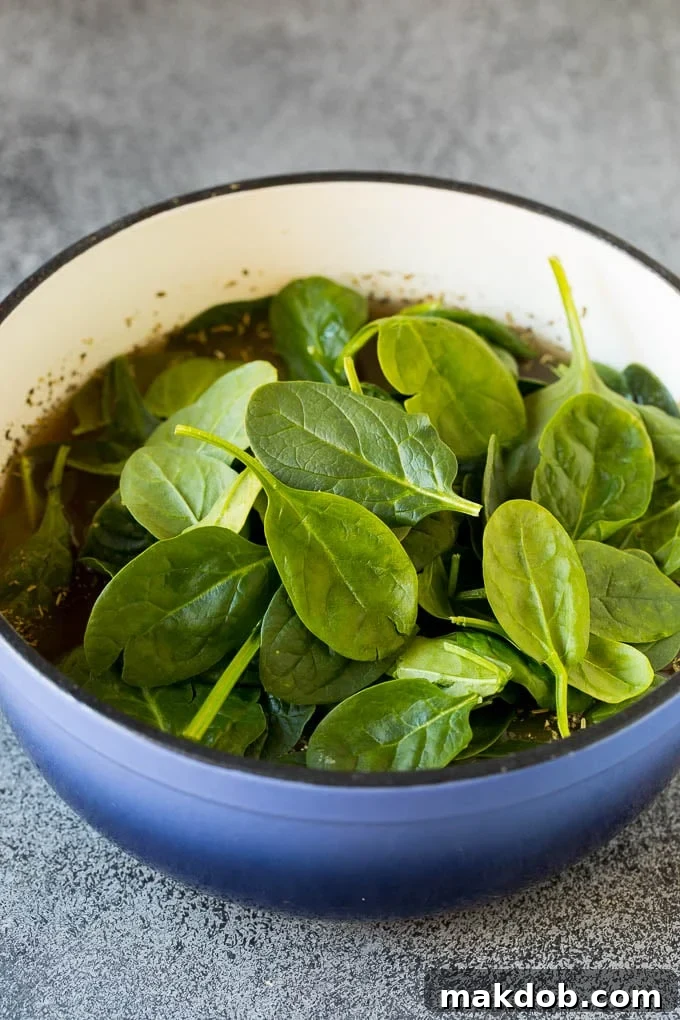 Spinach Wilting in Tuscan White Bean Soup A large pot of Tuscan white bean soup, with freshly added baby spinach leaves just beginning to wilt into the rich, savory broth, ready for serving.