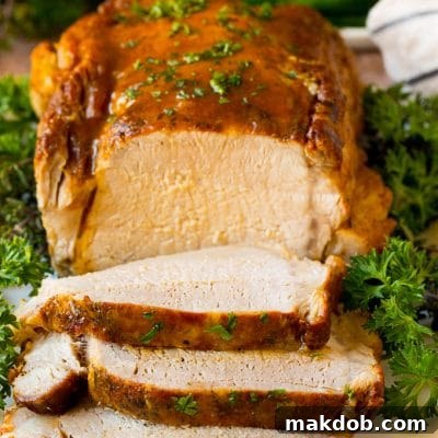 Slow Cooker Pork Perfection 2 Crock pot pork loin sliced on a serving plate, garnished with herbs.