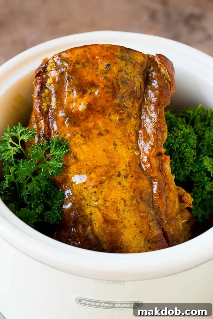 This crock pot pork roast is tender pork loin simmered in a slow cooker in a rich and flavorful gravy. Crock pot pork roast inside a slow cooker with gravy, garnished with fresh parsley.