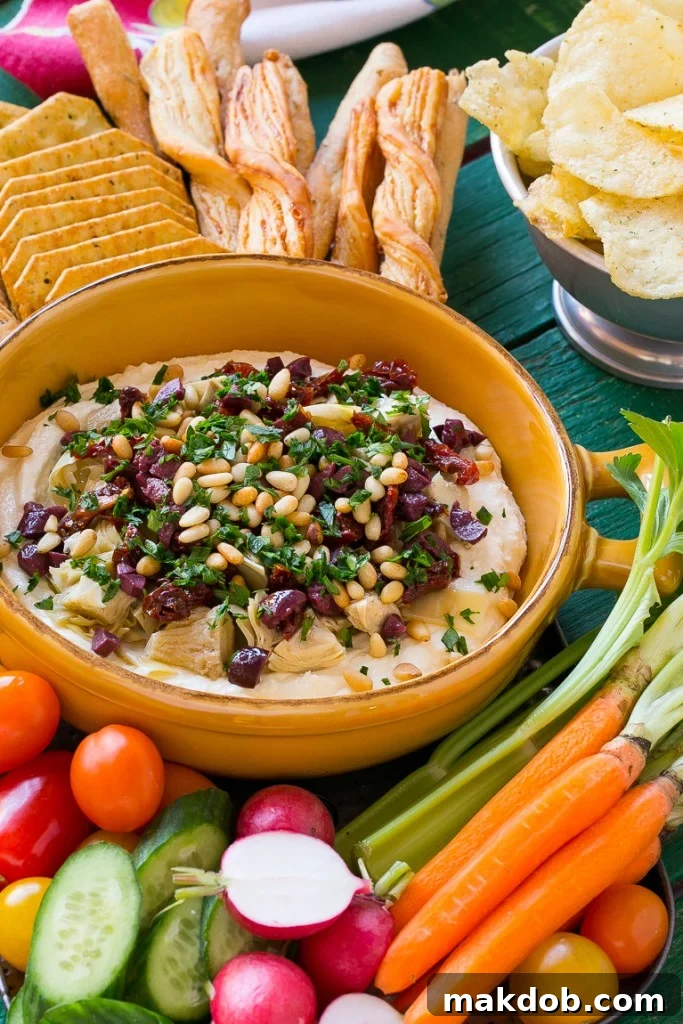 Close-up of a vibrant Mediterranean Layered Dip, garnished with fresh parsley and showcasing its distinct layers of whipped feta, sun-dried tomatoes, and olives. Perfect for serving with crisp crackers.