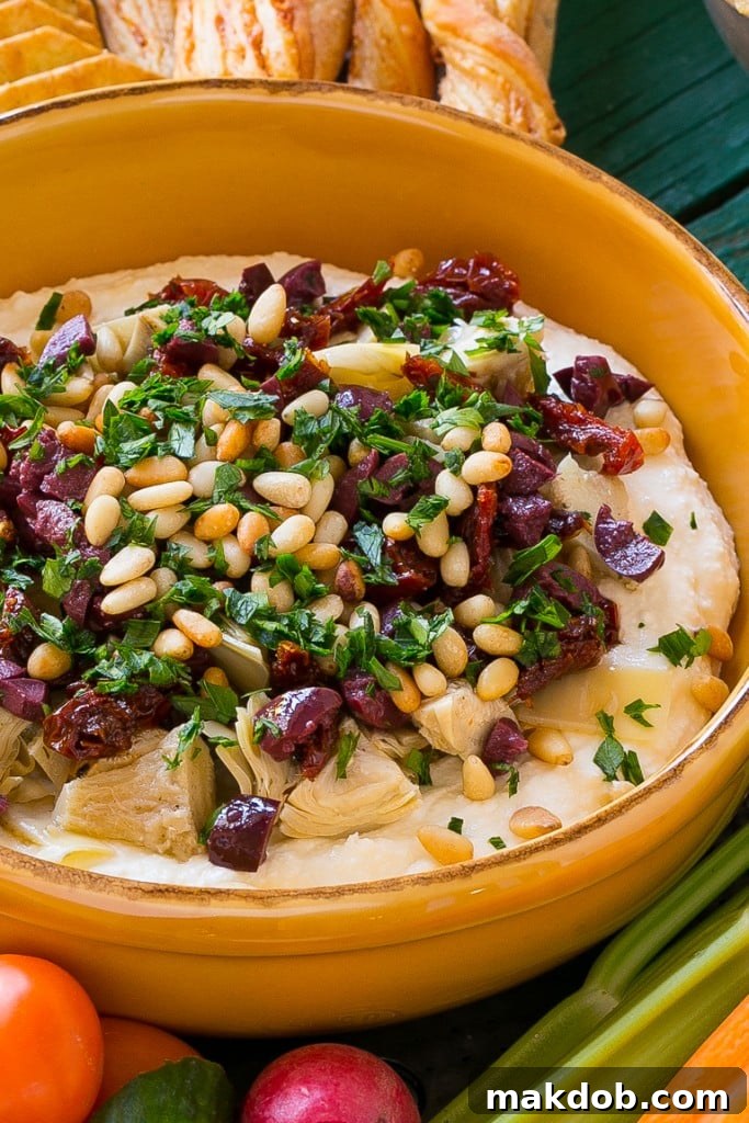 An overhead view of a beautifully prepared Mediterranean Layered Dip, ready for serving on a white platter, adorned with colorful toppings.