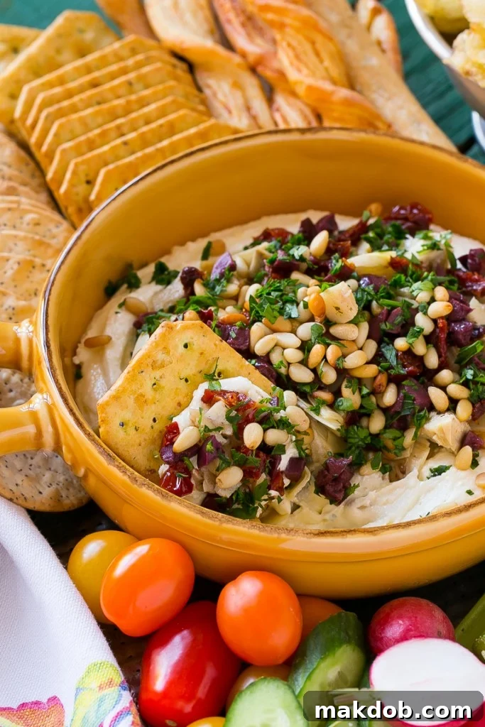 Close-up of Mediterranean Layered Dip artfully arranged with a variety of dippers including pita bread, crackers, and fresh vegetable sticks, emphasizing its party readiness.