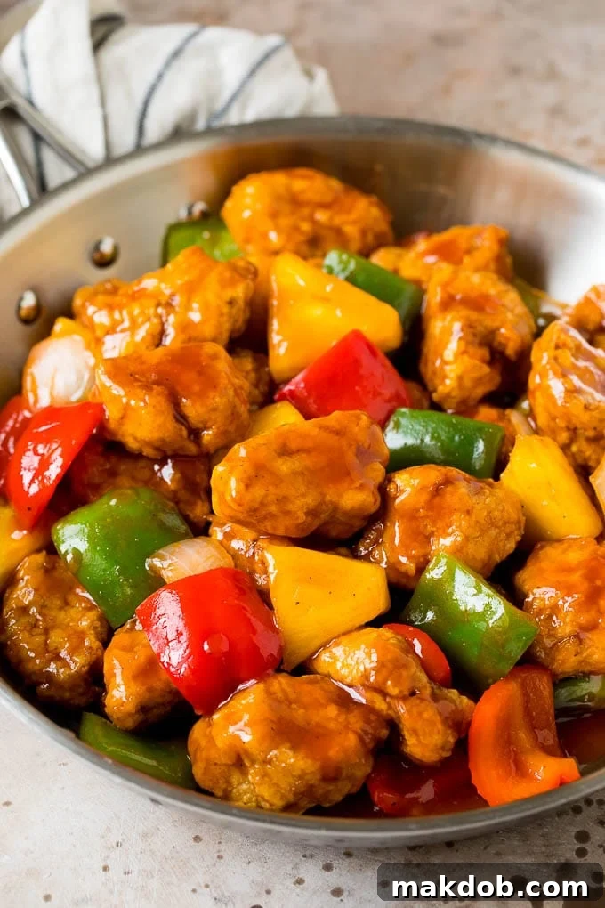A vibrant skillet of homemade sweet and sour pork, featuring golden-fried pork pieces, colorful bell peppers, and juicy pineapple chunks, all coated in a glistening red sauce.