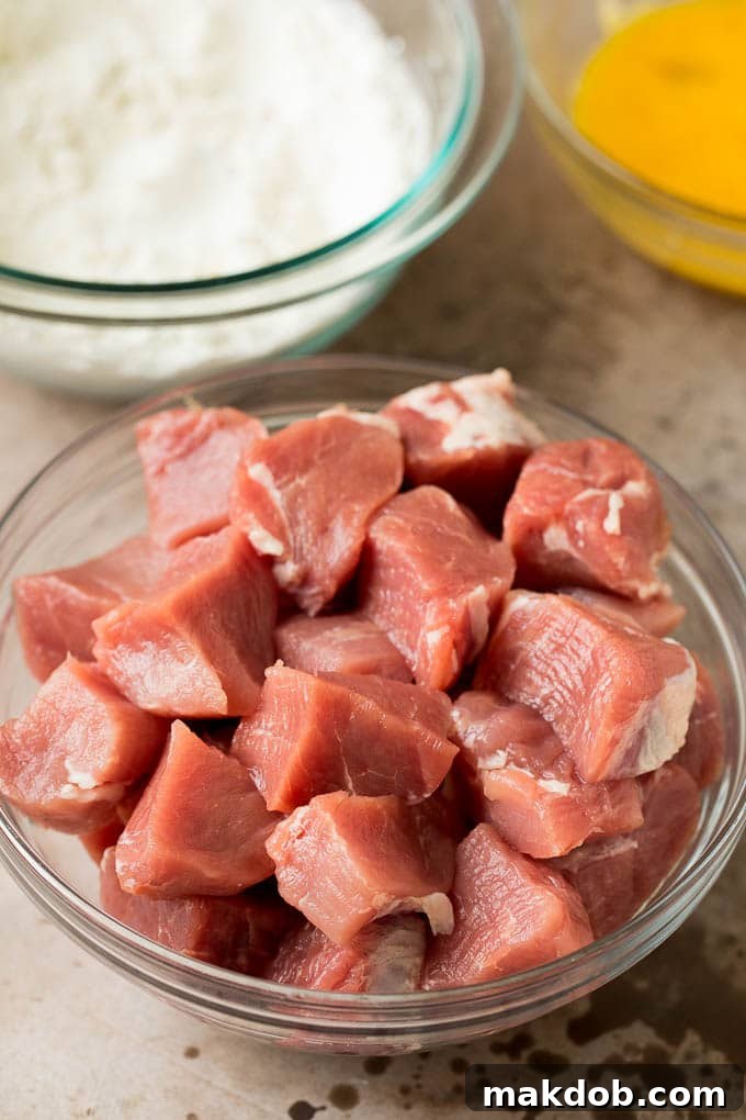 Cubes of pork tenderloin, a bowl of flour and a bowl of beaten eggs, ready for breading.