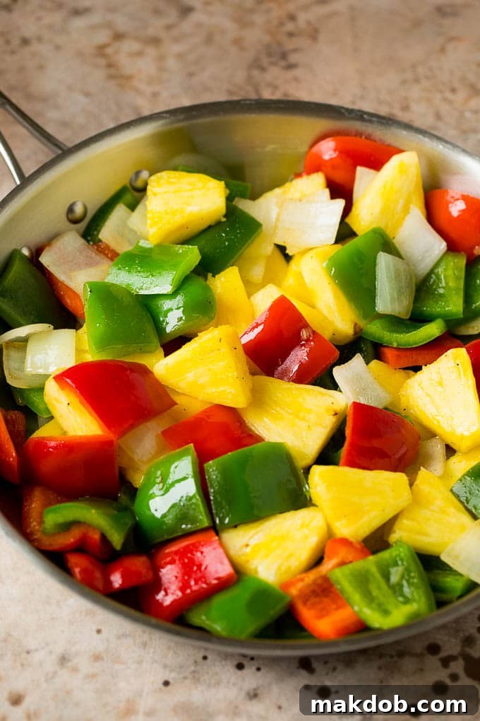 Pineapple chunks, red and green bell peppers, and onions sautéing in a pan.