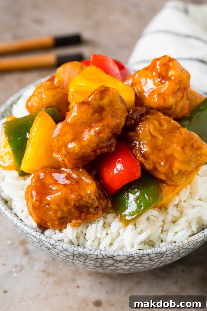 Sweet and sour pork served over a bed of white rice, garnished with green onions.