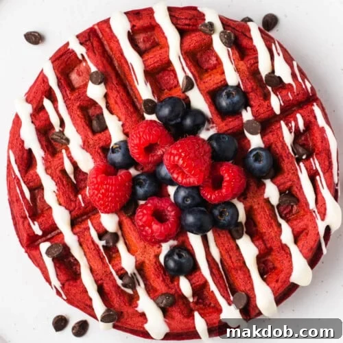 A stack of red velvet waffles topped with cream cheese icing and fresh berries.
