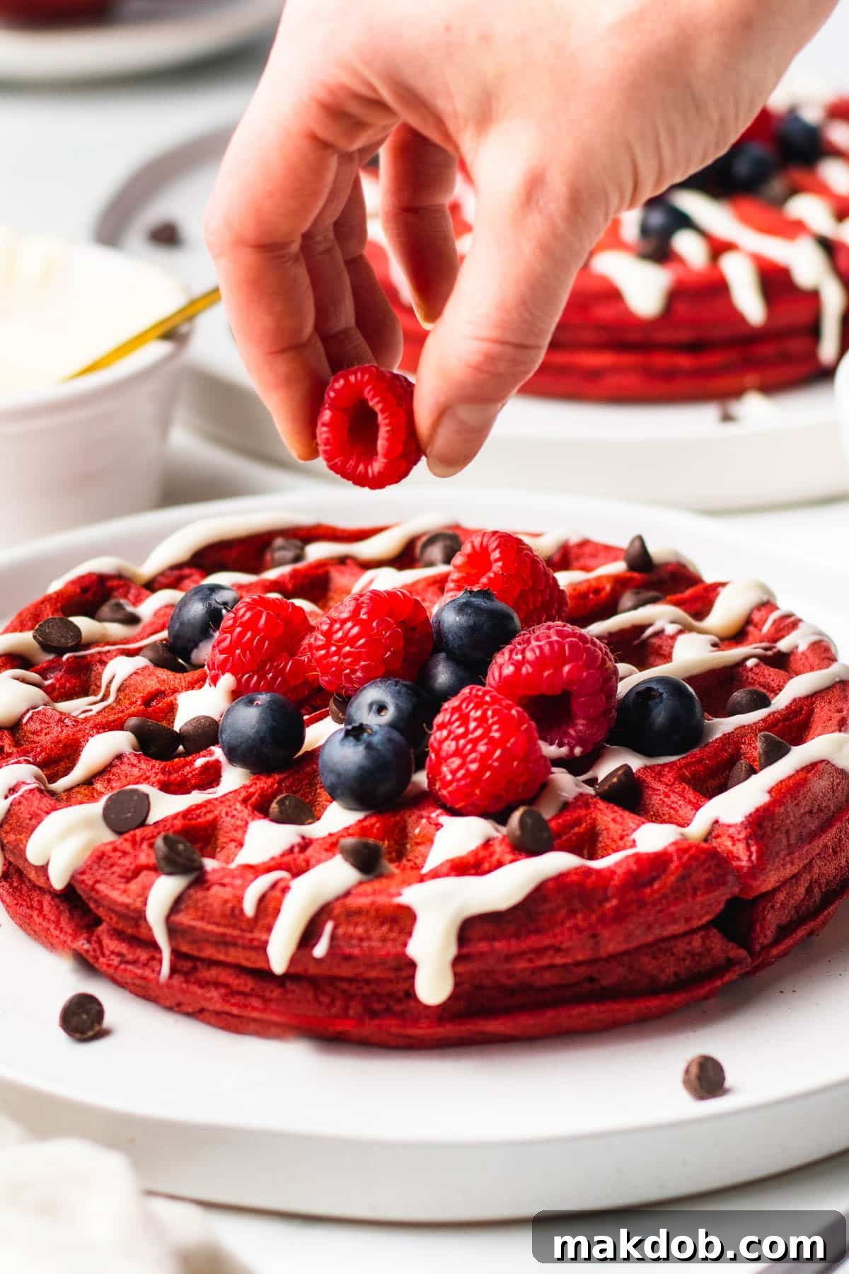 Crimson Velvet Waffles 6 A hand placing berries on top of red velvet waffles.
