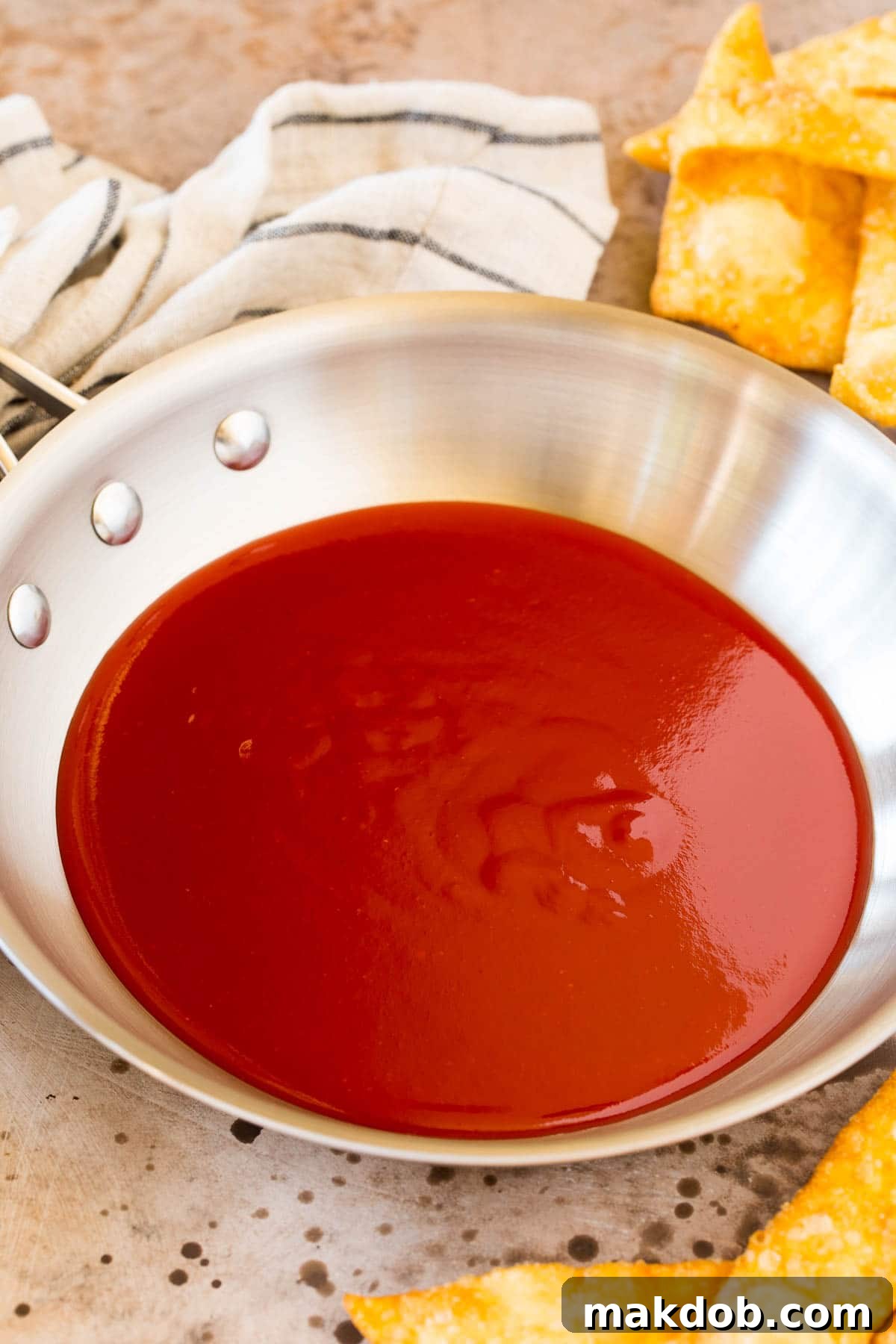 Sweet and Sour Sauce with Wontons A pan filled with luscious homemade sweet and sour sauce, surrounded by crispy fried wontons ready to be dipped and enjoyed.