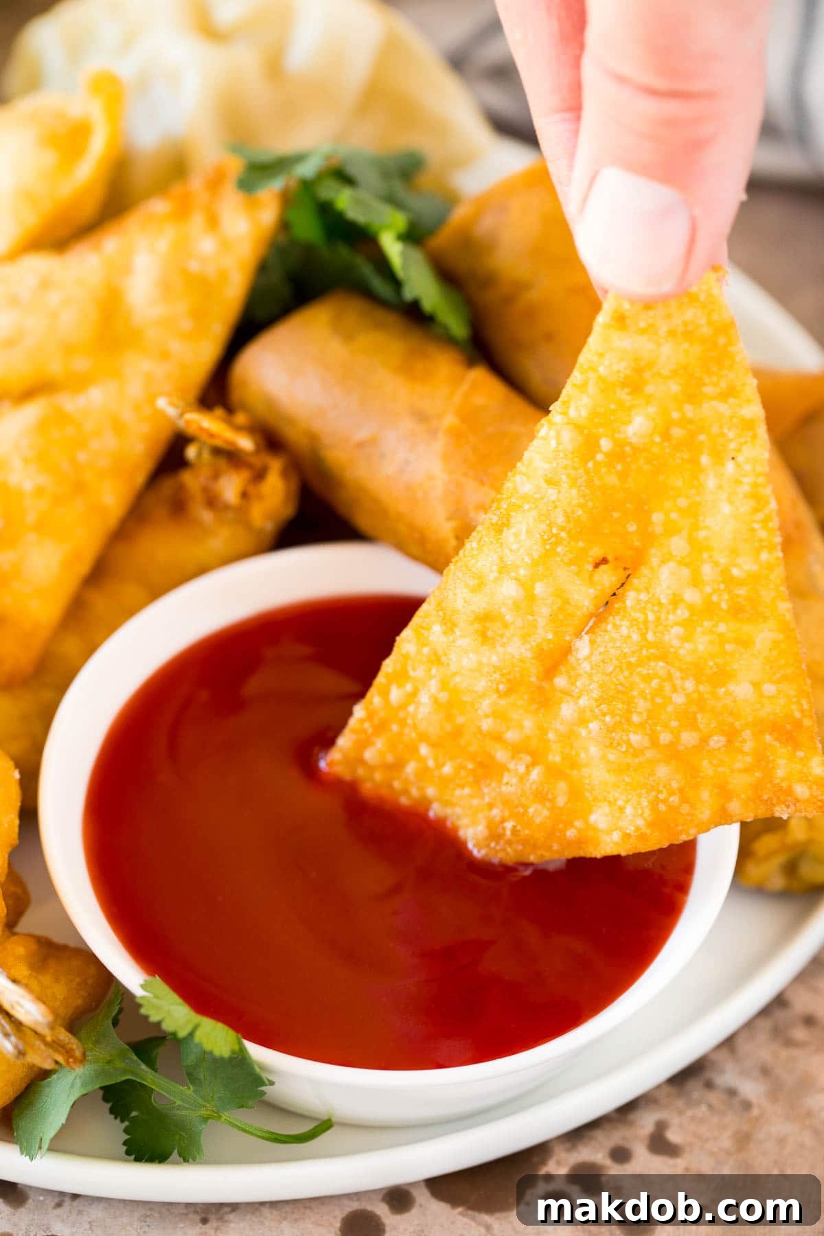 Wonton Dipped in Sweet and Sour Sauce A crispy fried wonton being gently dipped into a rich, vibrant bowl of homemade sweet and sour sauce, highlighting its perfect consistency.