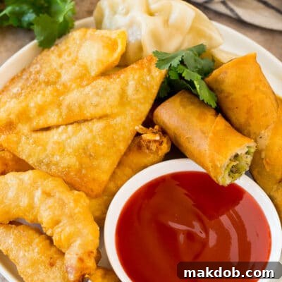 Zesty Sweet Harmony Sauce 3 A bowl of sweet and sour sauce served with egg rolls, shrimp and wontons.