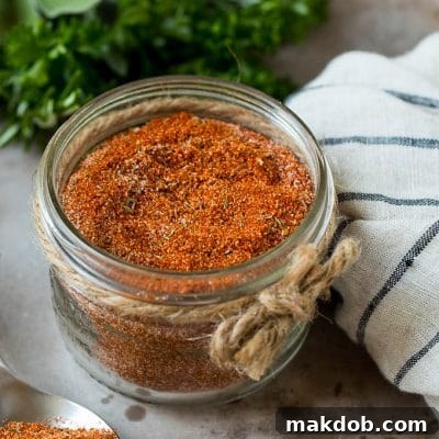 A jar of homemade blackened seasoning with fresh herbs in the background, perfect for adding zest to meals.