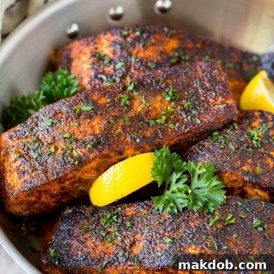 A pan of blackened salmon fillets garnished with lemon and parsley.