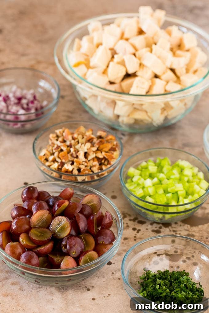 Bowls of diced chicken, celery, pecans, grapes, red onions and parsley, ready for mixing.