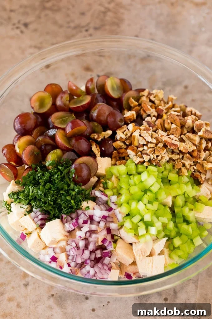 A mixing bowl with chicken, grapes, pecans, and red onions, ready for the dressing.
