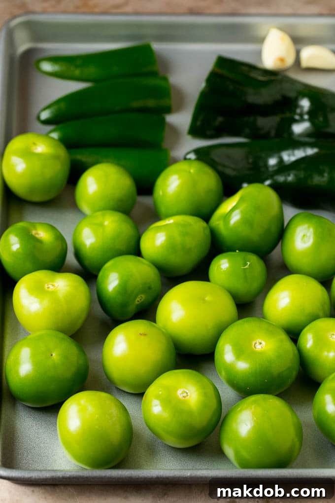 This homemade salsa verde is a combination of roasted chilies, tomatillos, garlic, cilantro and lime juice, all blended together to make a light and refreshing dip. Tomatillos and halved peppers on a sheet pan, perfectly roasted and ready for blending.