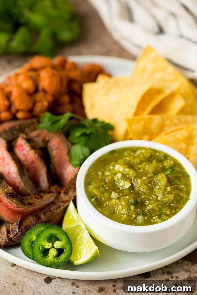 This homemade salsa verde is a combination of roasted chilies, tomatillos, garlic, cilantro and lime juice, all blended together to make a light and refreshing dip. Salsa verde served with carne asada, beans and tortillas, showcasing its versatility as a side dish.