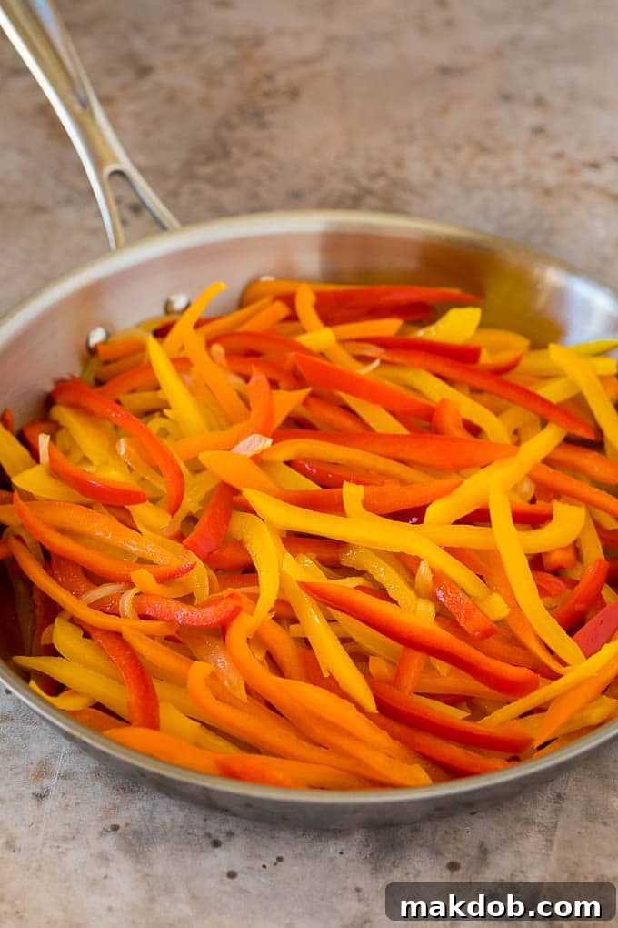 Sautéing bell peppers and onions for peperonata Vibrantly sliced red, yellow, and orange bell peppers, alongside thinly sliced onions, gently cooking in a pan to prepare a savory peperonata.
