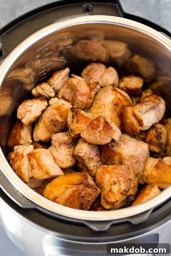Seared pork pieces cooking in an Instant Pot, surrounded by savory juices.