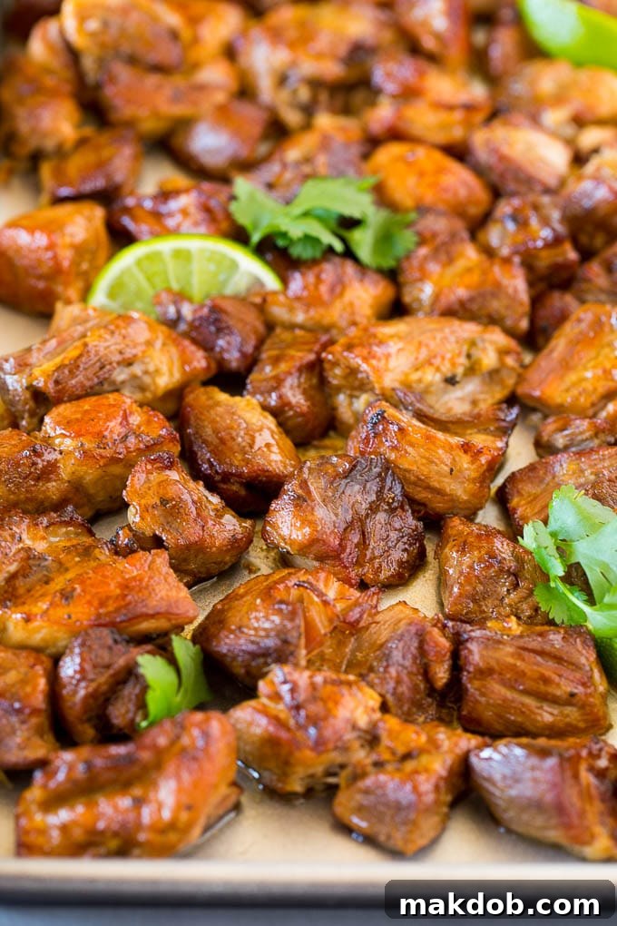 A sheet pan of crispy Instant Pot carnitas garnished with fresh lime wedges and cilantro.