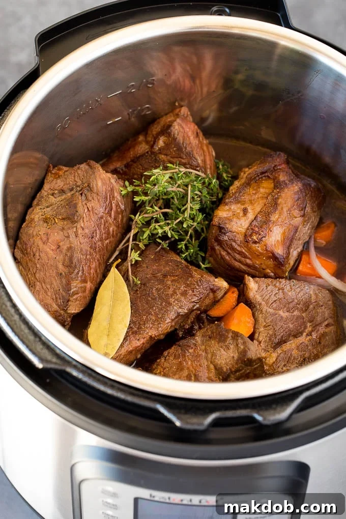 A pressure cooker filled with Instant Pot short ribs, herbs, vegetables and beef broth.
