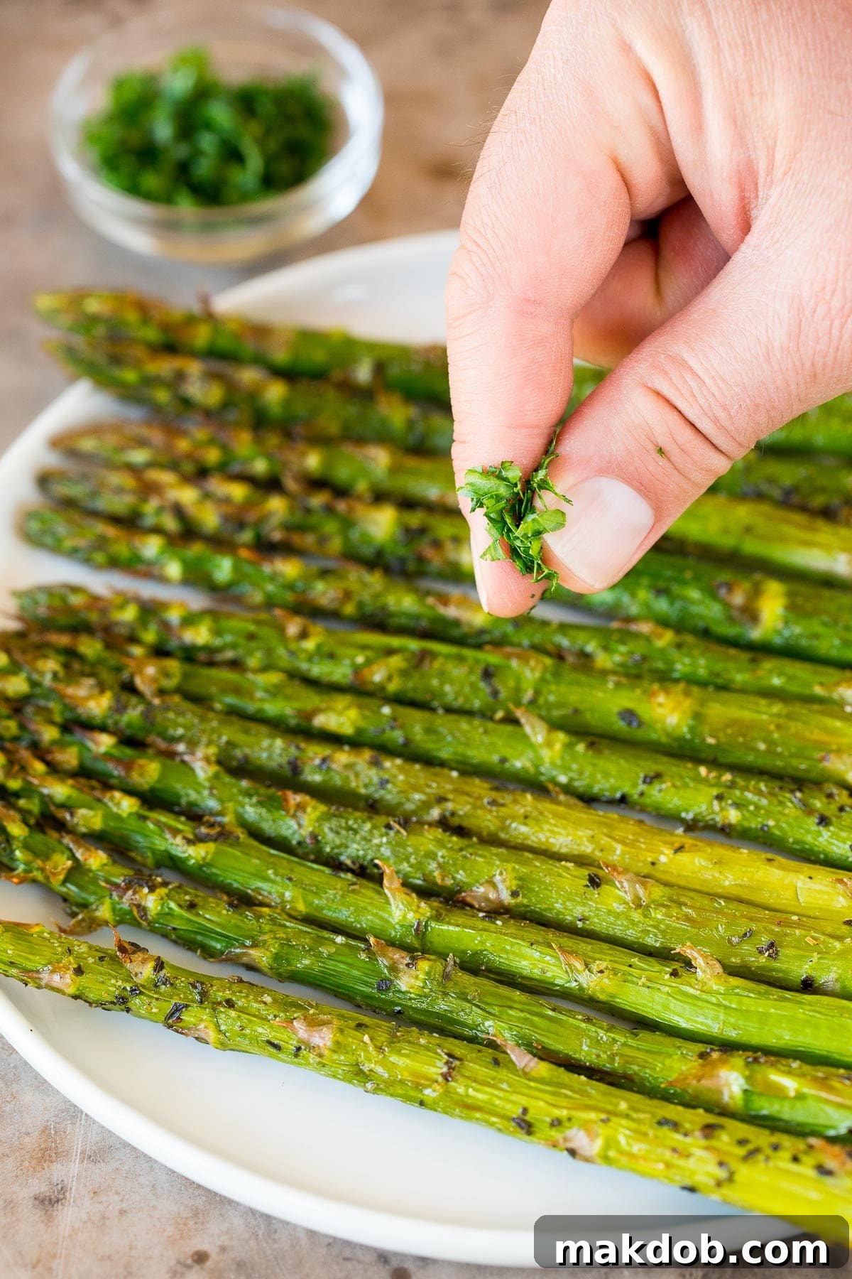 Parsley being sprinkled over a plate of cooked asparagus.