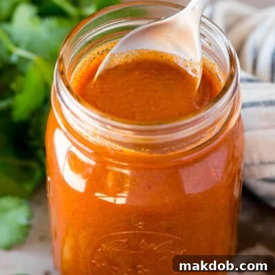 Authentic Enchilada Sauce from Your Kitchen 2 A jar of homemade enchilada sauce with a spoon in it.