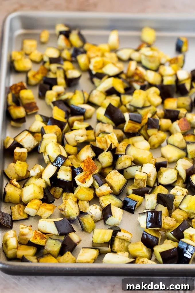 Perfectly roasted eggplant cubes, golden brown and tender, scattered on a parchment-lined baking sheet, demonstrating the ideal preparation for the base of a delicious caponata.