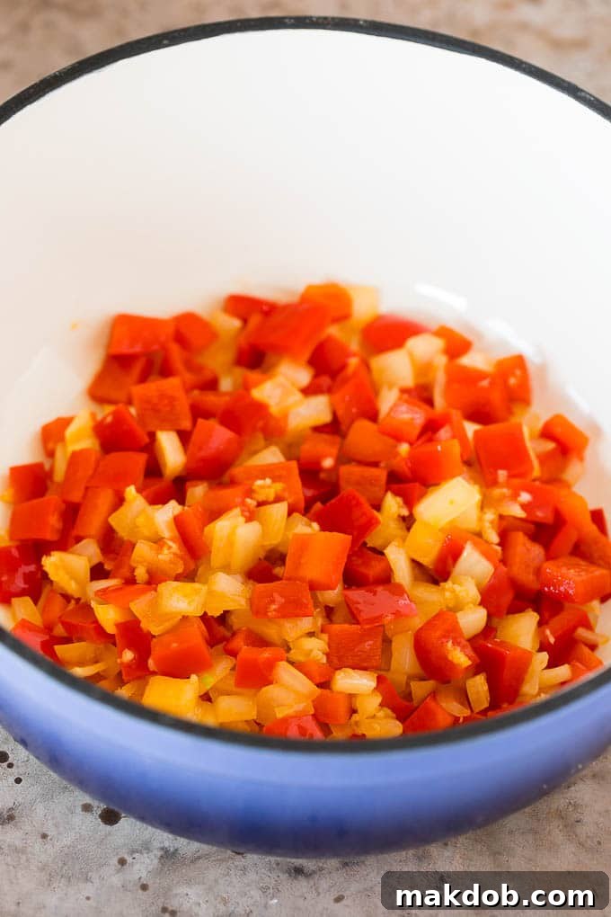 Sautéing Onions and Peppers for Chili Vibrant red bell peppers and chopped onions gently sautéing in a large pot with olive oil, forming the aromatic foundation of the chili.