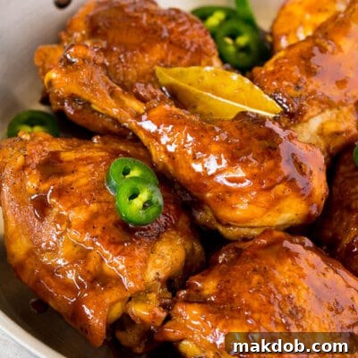 A pan of chicken adobo garnished with sliced jalapeno.