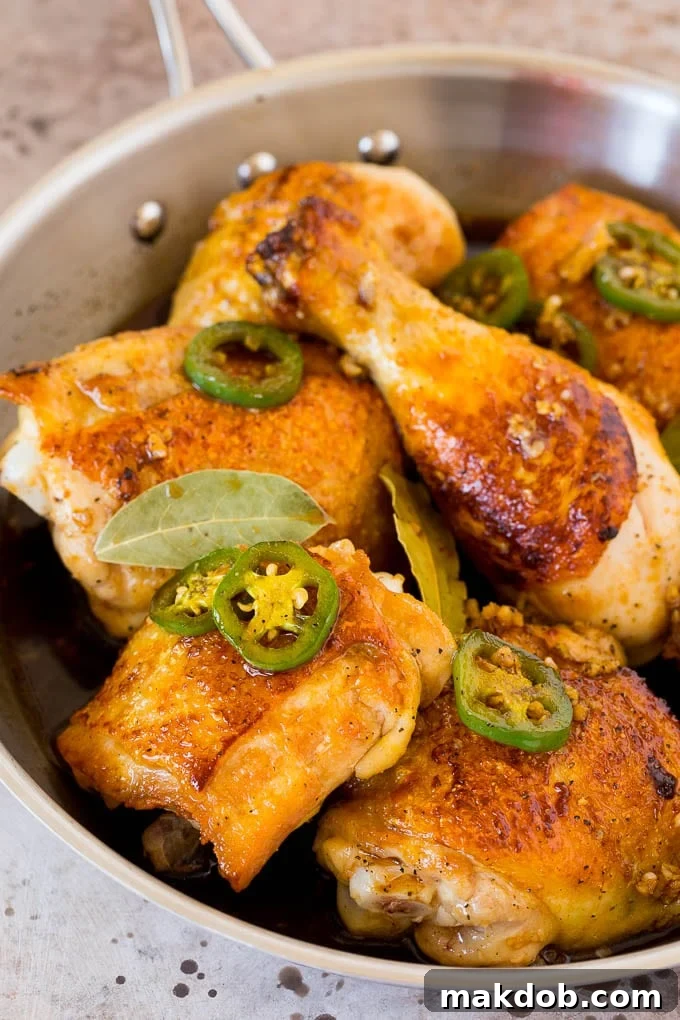 This chicken adobo is a Filipino dish made with chicken pieces simmered in a sweet and savory sauce. An easy dinner option with minimal ingredients that always gets rave reviews! A pan of chicken with jalapenos, soy sauce and garlic.