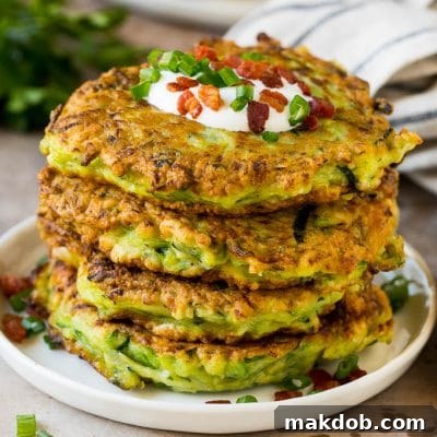 A stack of zucchini fritters topped with sour cream and bacon.