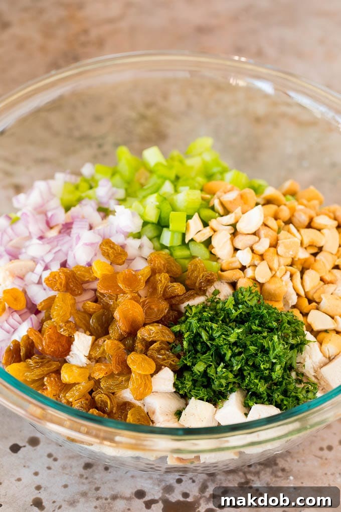 A bowl of diced chicken with golden raisins, roasted cashews, minced celery, and chopped red onion, perfectly prepped for curry chicken salad.