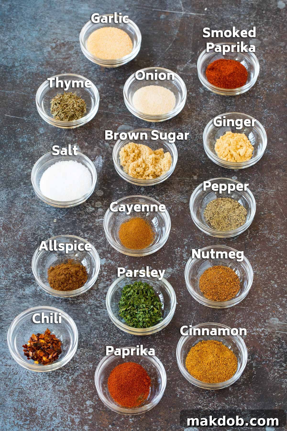 Small glass bowls meticulously arranged with various herbs and spices, showcasing the vibrant components of homemade Jamaican jerk seasoning.