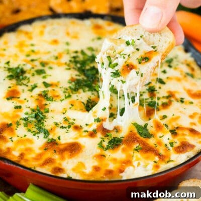 Irresistible Artichoke Dip 7 A skillet of artichoke dip with a hand reaching to take a serving.