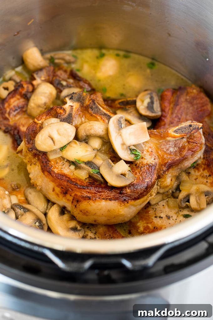 These Instant Pot pork chops are seared to golden brown perfection, then pressure cooked and covered in mushroom gravy. A pot of pork chops topped with mushrooms.