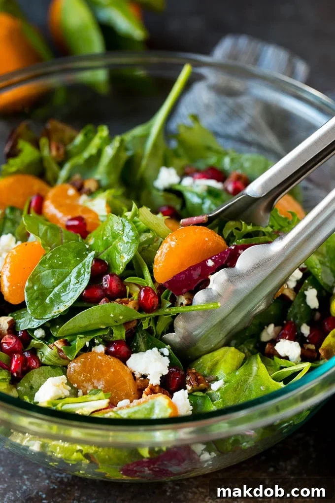 Tongs serving up a portion of Christmas salad, showcasing its vibrant ingredients.