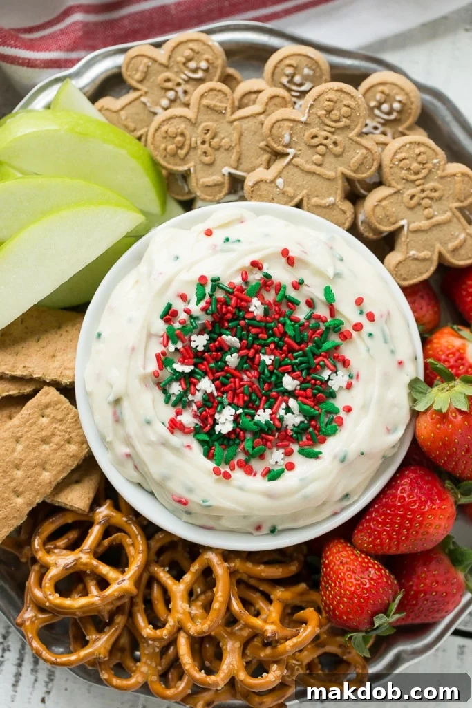 Magical Christmas Cookie Dough Dip 2 A festive red and green Christmas Cookie Dough Dip, topped with sprinkles, served in a white bowl with various dippers like fruit, graham crackers, and cookies around it.