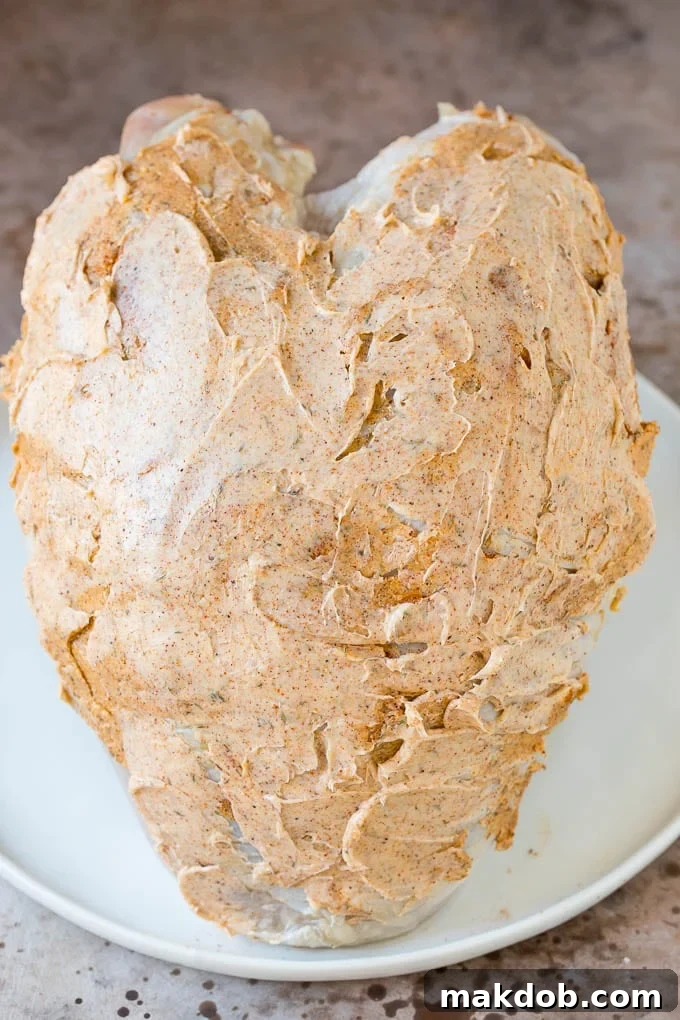 Uncooked turkey breast generously coated in seasoned butter.