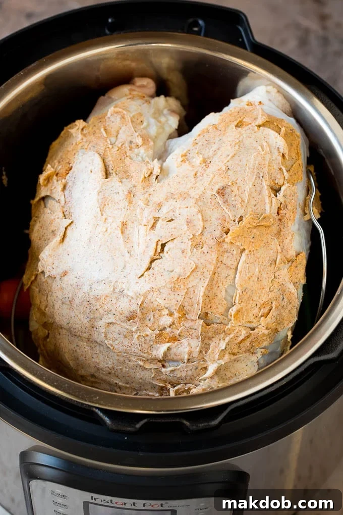 A butter coated turkey breast placed inside a pressure cooker on a trivet.