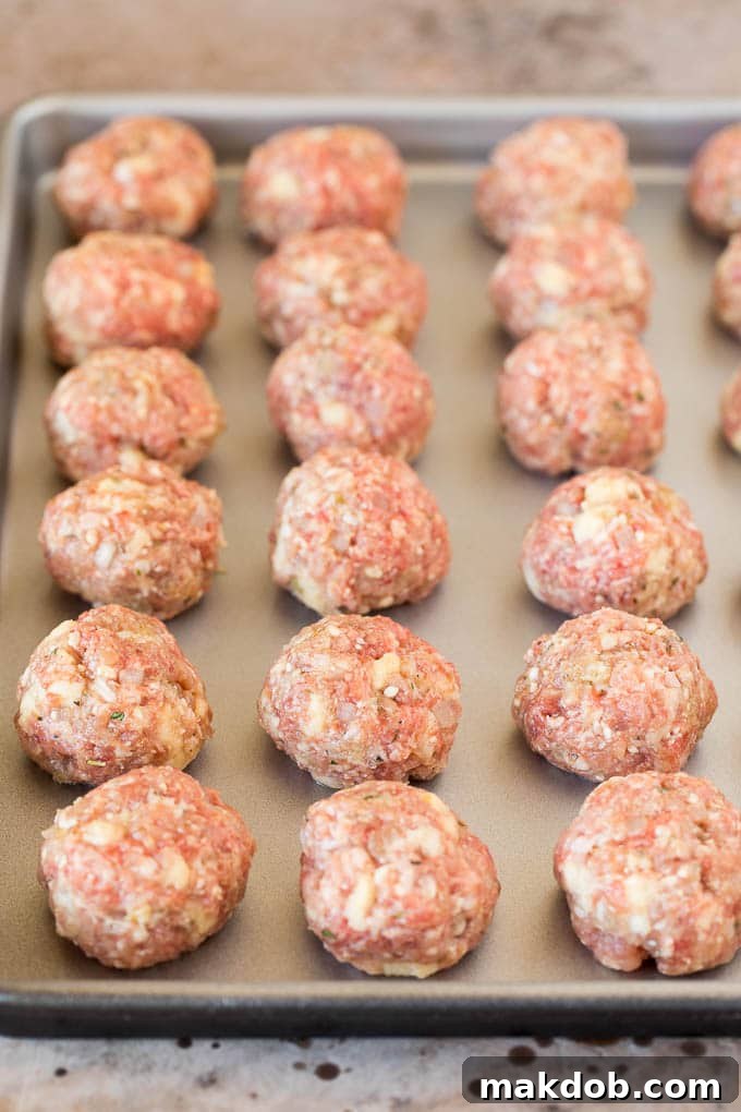 Raw, perfectly shaped Italian meatballs resting on a baking sheet, ready for cooking.
