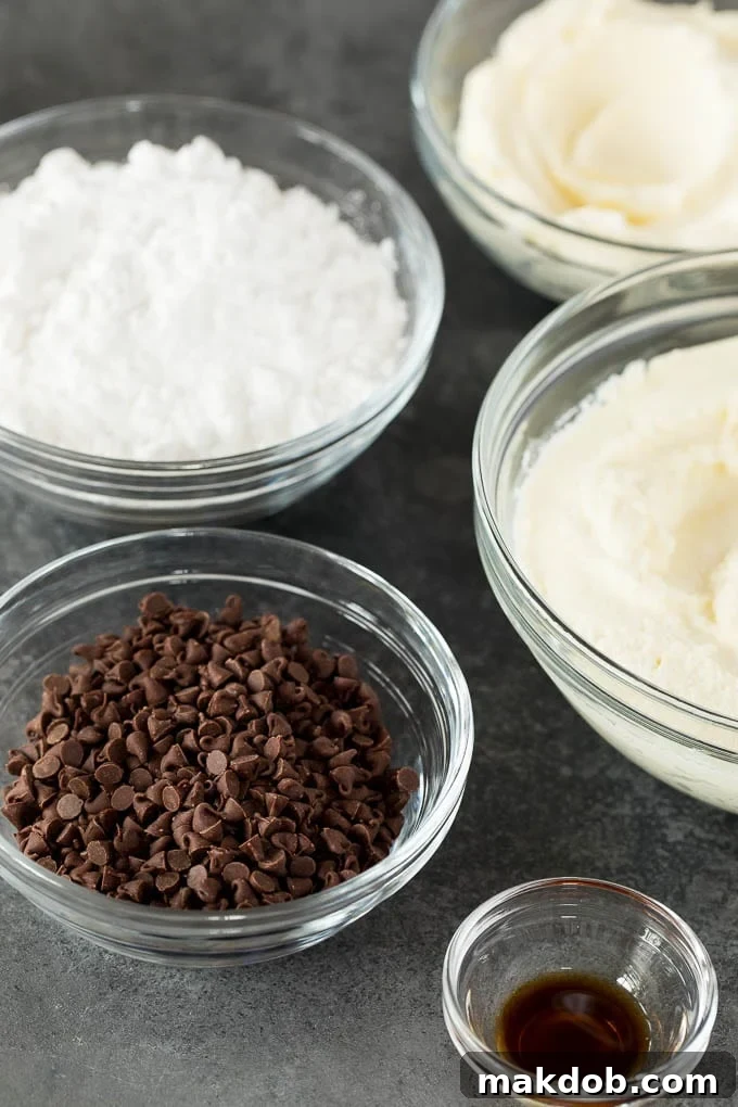 This cannoli dip is a blend of two types of sweet Italian cheeses, sugar and chocolate chips, all blended together to make a creamy dip that tastes just like the inside of a cannoli. Various cannoli dip ingredients laid out in small bowls: miniature chocolate chips, creamy ricotta cheese, smooth mascarpone cheese, fluffy powdered sugar, and a vial of rich vanilla extract, ready for mixing.