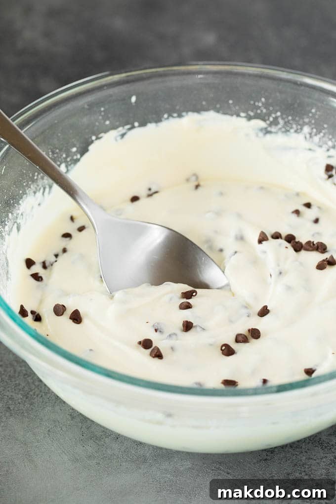 This cannoli dip is a blend of two types of sweet Italian cheeses, sugar and chocolate chips, all blended together to make a creamy dip that tastes just like the inside of a cannoli. A pristine glass bowl showcasing a perfectly smooth and creamy cannoli dip, a delightful mixture of sweet Italian cheeses, powdered sugar, and miniature chocolate chips, ready for presentation.