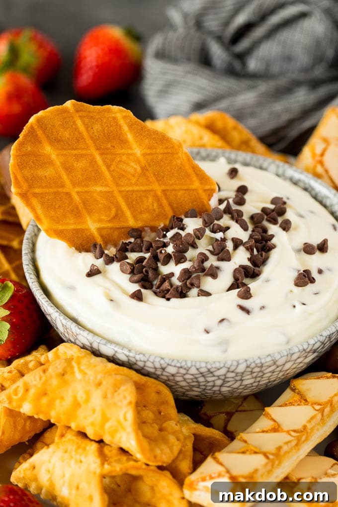 This cannoli dip is a blend of two types of sweet Italian cheeses, sugar and chocolate chips, all blended together to make a creamy dip that tastes just like the inside of a cannoli. A bowl of creamy cannoli dip with a waffle cookie nestled inside, demonstrating one of the many delicious ways to enjoy this easy Italian dessert.