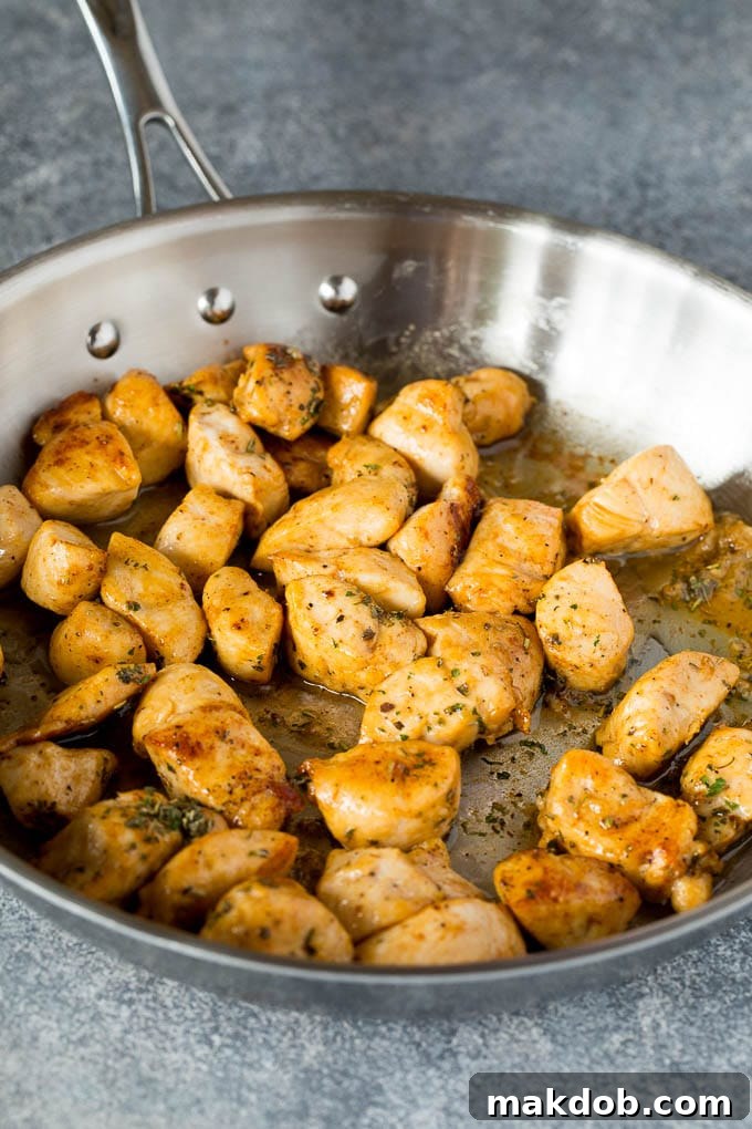 Diced and cooked golden-brown chicken breast pieces resting in a non-stick skillet after sautéing, seasoned with herbs.