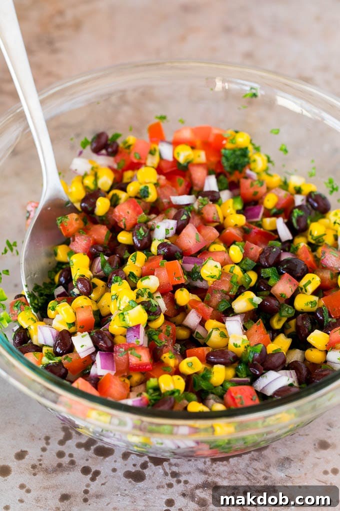 Corn, beans, tomatoes and seasonings mixed together in a glass bowl.