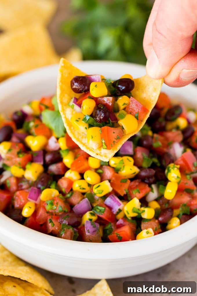 A hand holding a chip topped with black bean and corn salsa.
