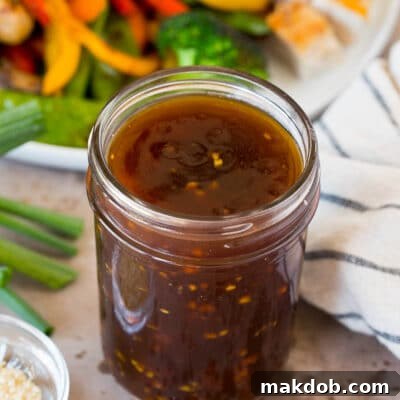 A jar of teriyaki sauce shown next to a plate of vegetables and chicken.