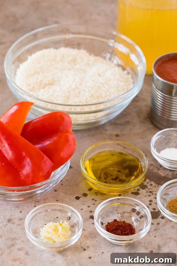 Individual bowls holding separate ingredients for Mexican rice, including uncooked rice, quartered red bell pepper, olive oil, and a mix of chili powder, cumin, and minced garlic.